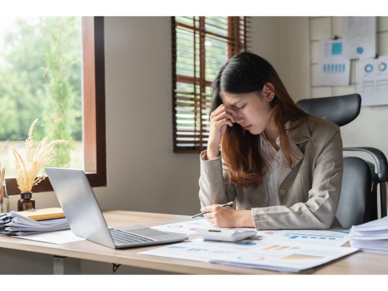 Focused and stressed businesswoman working on a project while at her desk, surrounded by documents and using a laptop, lamenting how her attorney screwed up her case.