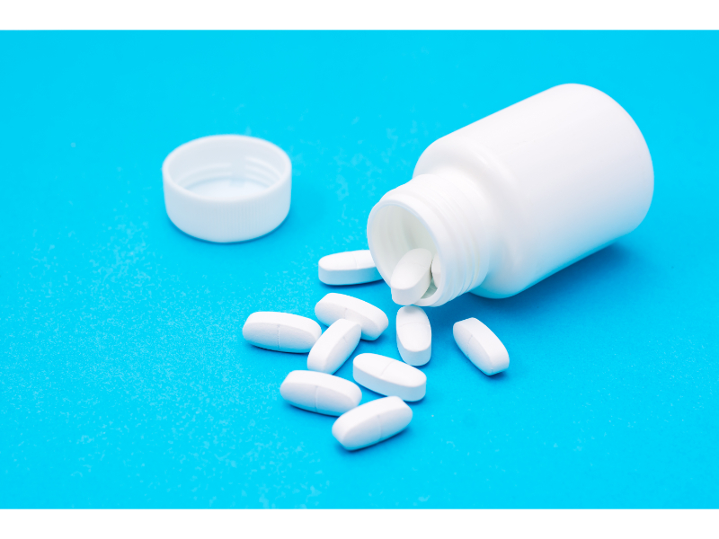 White Tylenol pills spilled from an open bottle onto a blue surface.