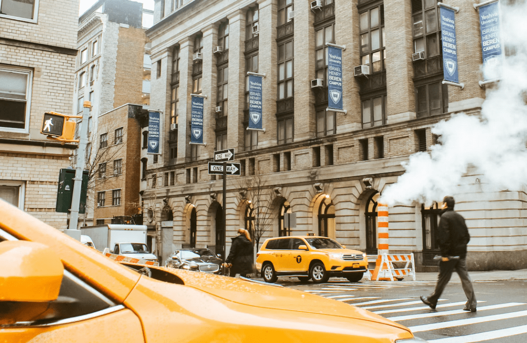 a man walking across a street next to a yellow car.