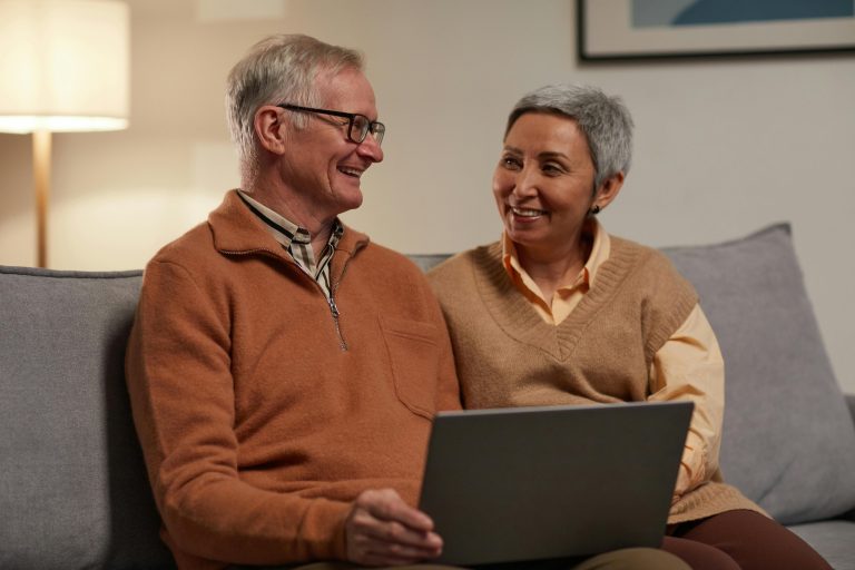 Mature couple smiling at one another using a computer